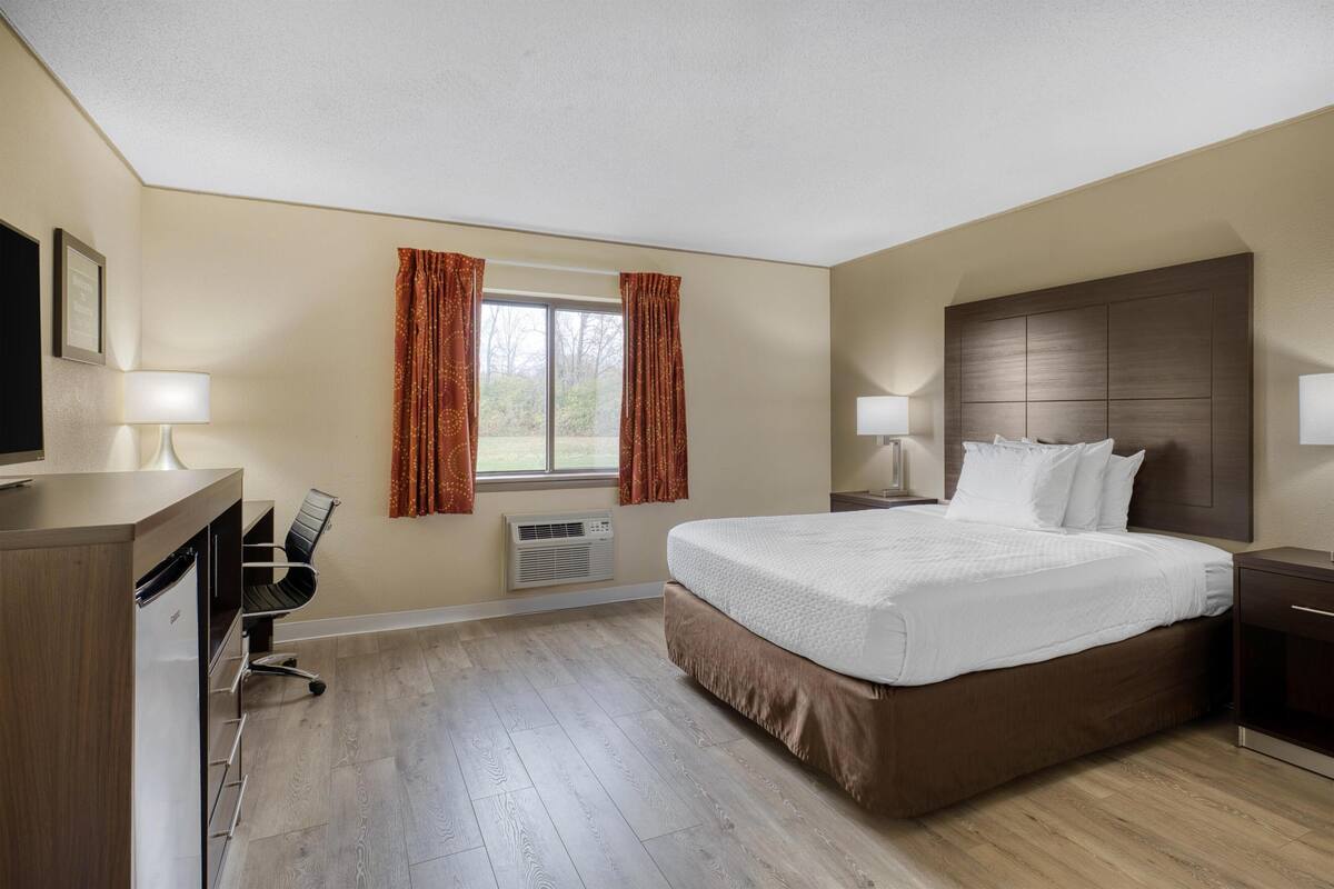 Een hotelkamer met een groot bed, een bureau met stoel, een televisie en een raam met gordijnen.