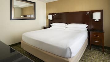 Una habitación de hotel con una cama grande, dos mesitas de noche, un tocador, un espejo y piso alfombrado.