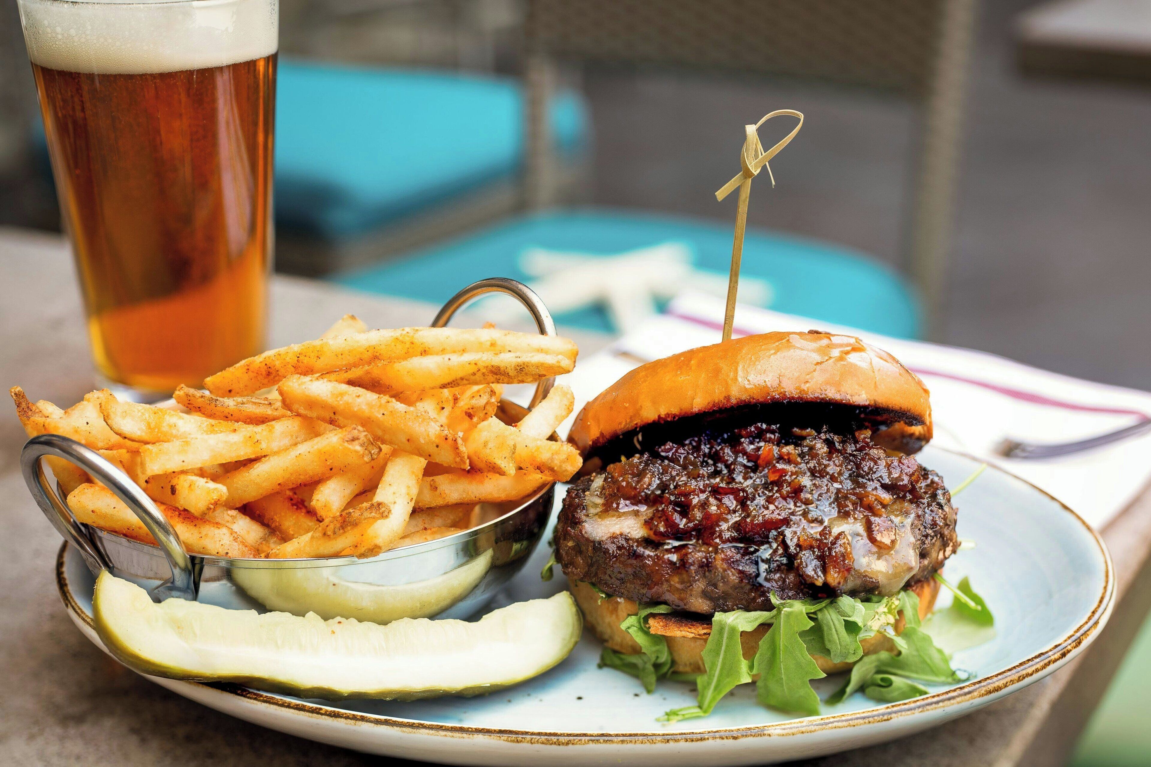 A meal consisting of a burger, fries, and a drink, served on a plate with a side of pickles.