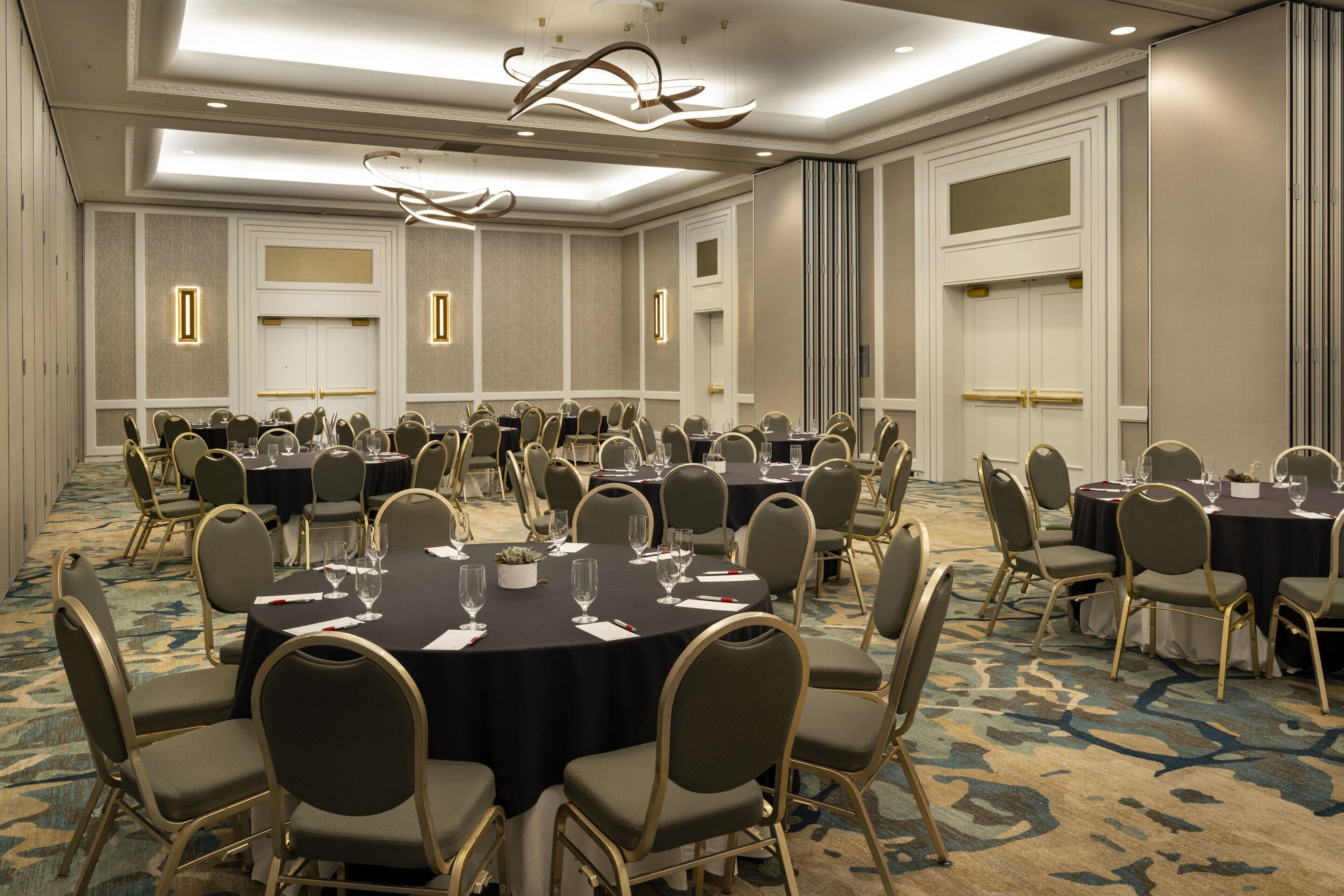 A conference room with multiple round tables and chairs, equipped with glassware and place settings.