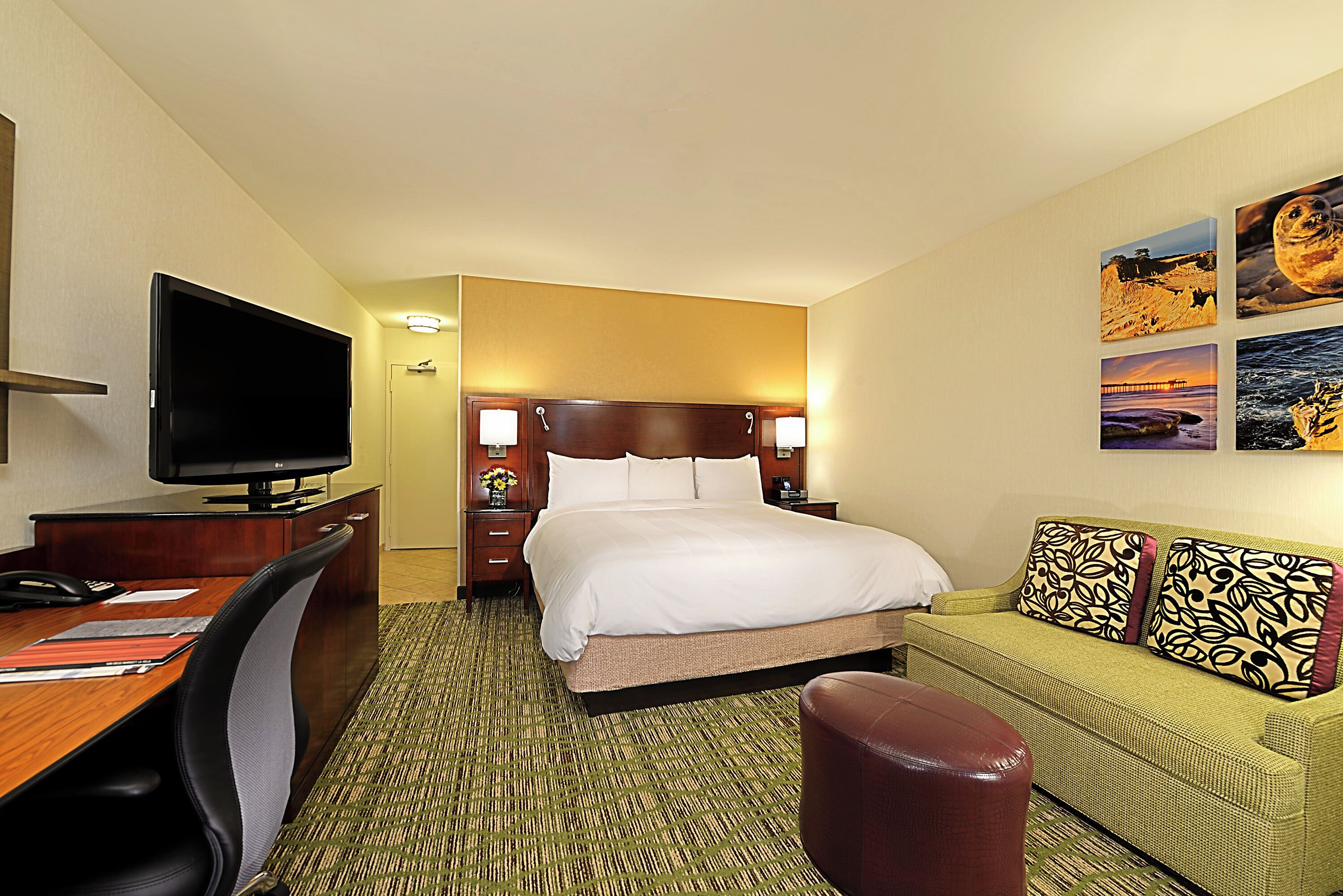 Ein Hotelzimmer mit Bett, Schreibtisch mit Fernseher, Sofa und Kunstwerk an der Wand.