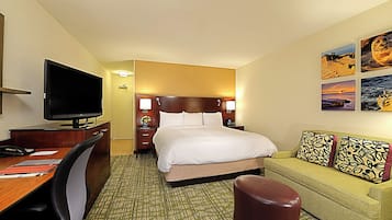 Ein Hotelzimmer mit Bett, Schreibtisch mit Fernseher, Sofa und Kunstwerk an der Wand.