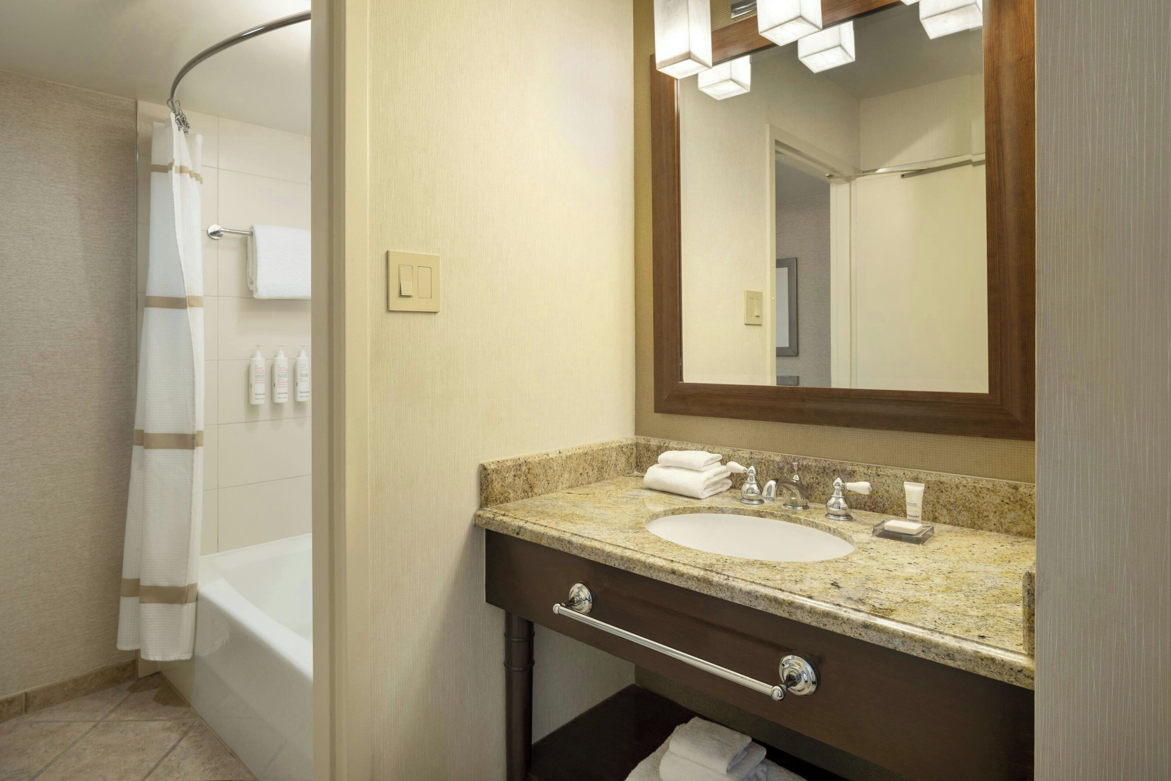 A bathroom with a bathtub, a sink with a vanity, a mirror, and a shower curtain.