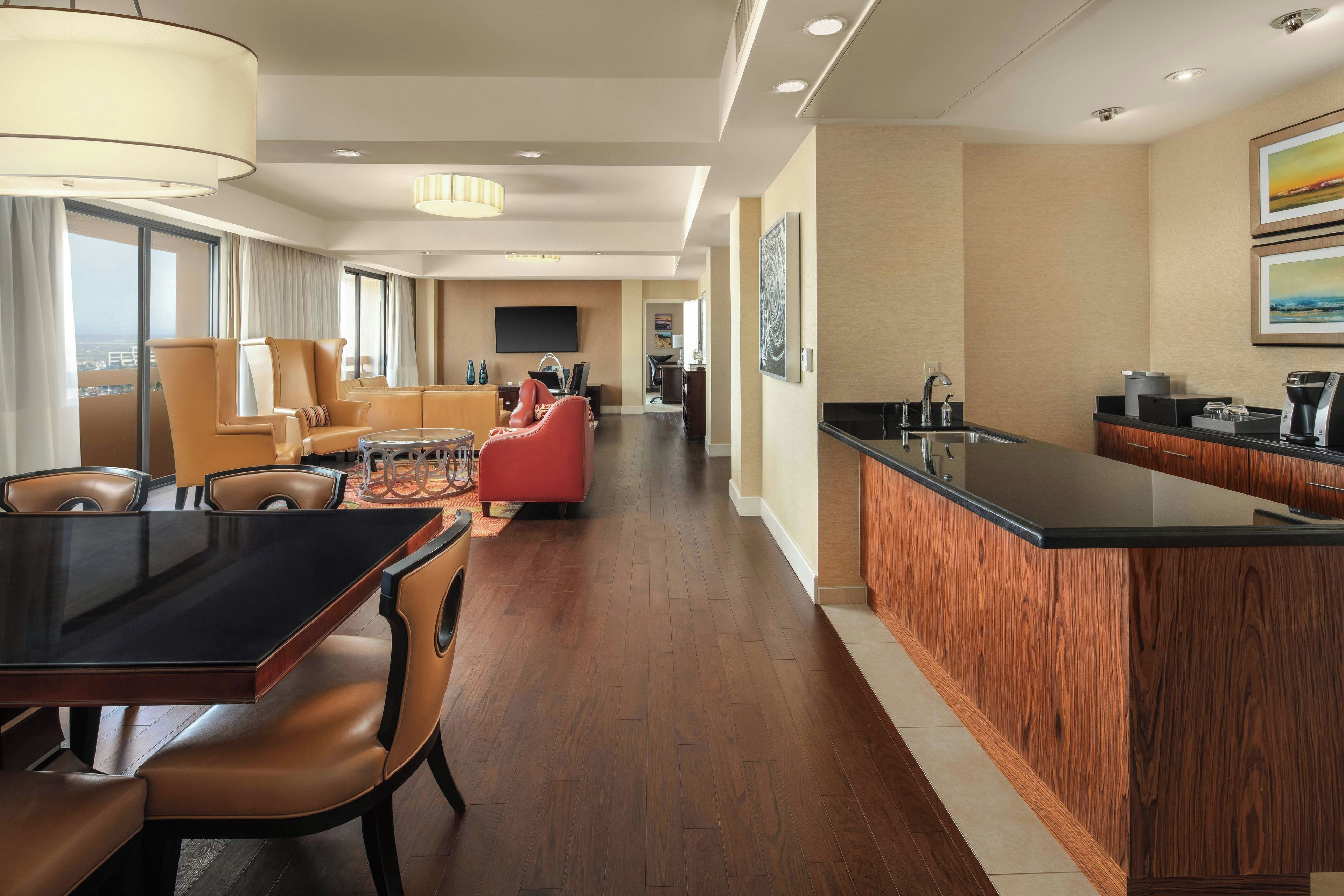 A modern hotel room with a dining area, a kitchen, and a living room.