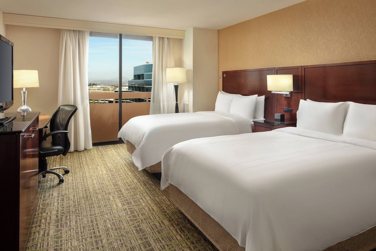 Ein Hotelzimmer mit zwei Betten, einem Schreibtisch mit Stuhl, einem Fernseher und Blick auf die Stadt.