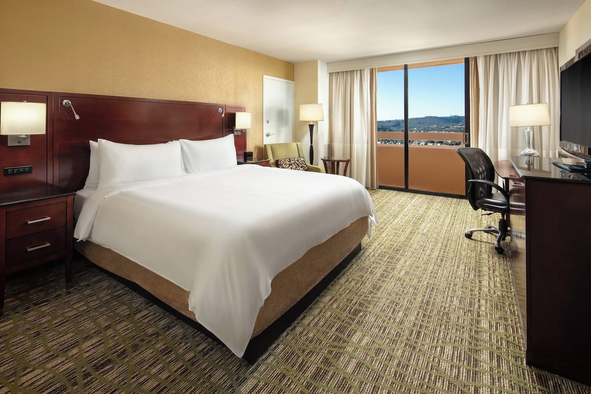 Ein Hotelzimmer mit einem großen Bett, einem Schreibtisch, einem Sessel und Blick auf die Stadt.
