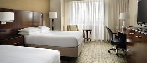 A hotel room with two beds, a desk, a chair, a television, and a window with curtains.