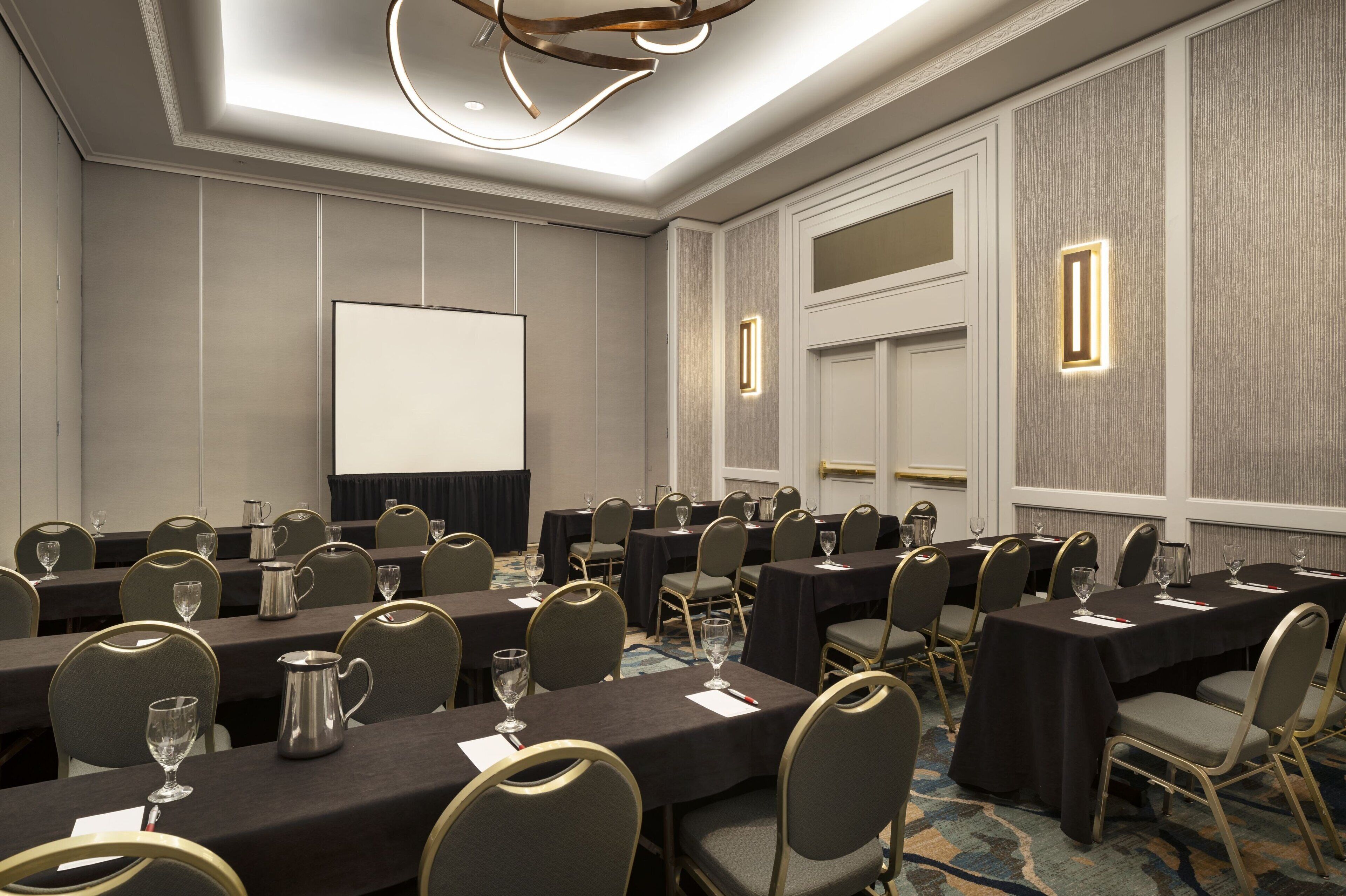 A conference room with tables, chairs, and a projector screen.