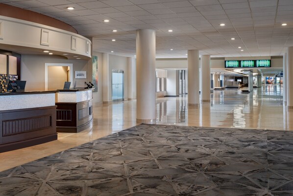 A spacious lobby with a reception desk, a digital display board, and a patterned floor. - Tampa Airport Marriott (Tampa)