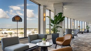 Un vaste espace salon doté de grandes fenêtres, de sièges confortables et offrant une vue sur l’aéroport.