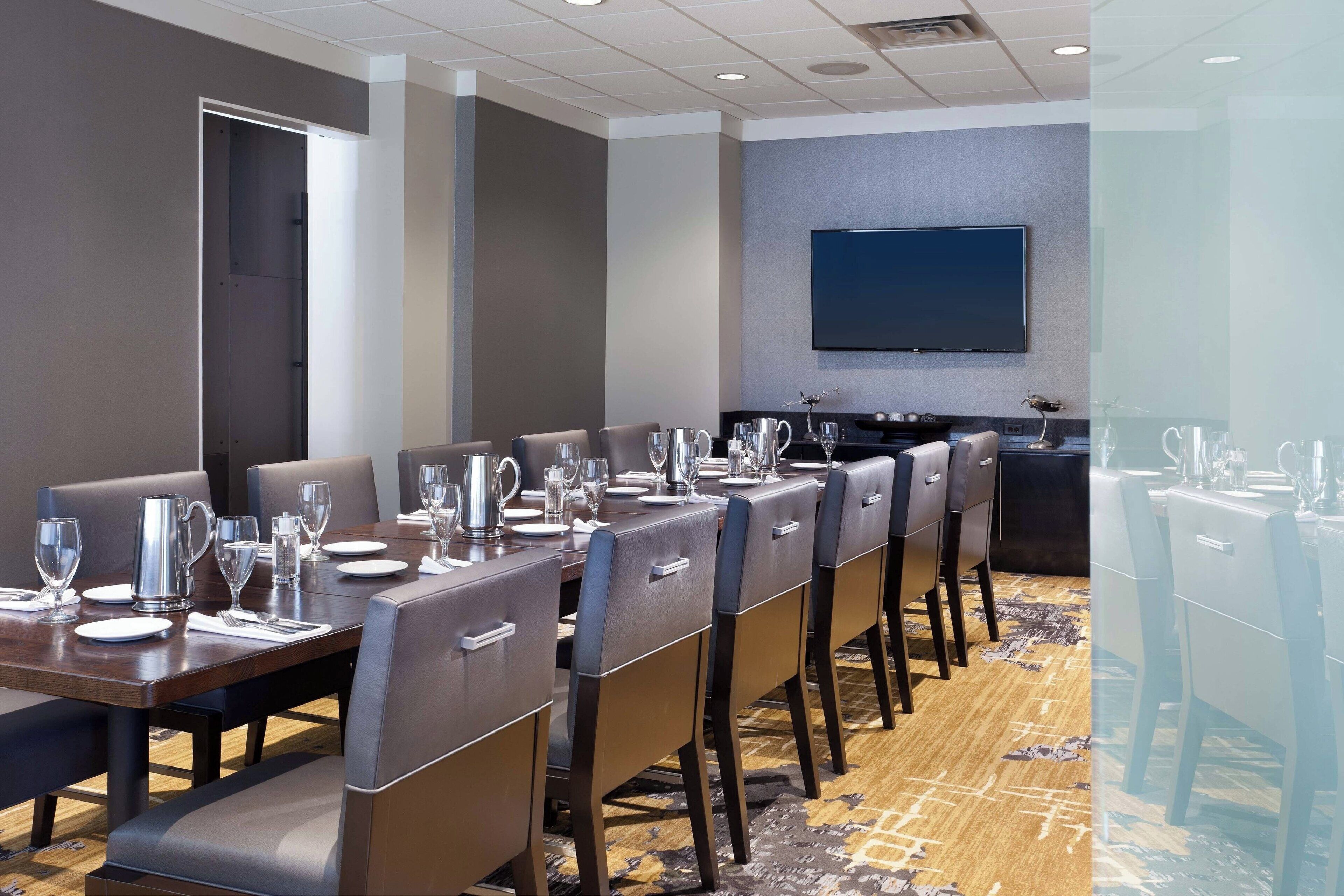 A conference room with a long table set for a meeting, equipped with chairs, a projector, and a screen.