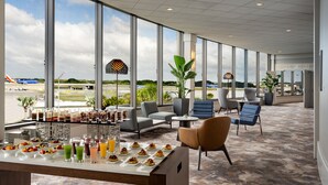 Un vaste espace de détente avec un buffet, des sièges confortables et de grandes fenêtres donnant sur la vue de l’aéroport.