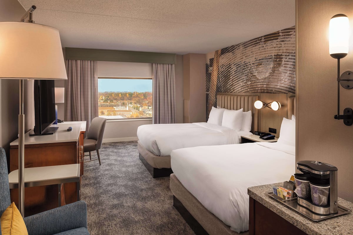 Quarto de hotel com duas camas, uma escrivaninha, uma cadeira, uma máquina de café e vista para a cidade.