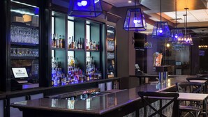 En bar med minibar, hylder med flasker og hængende blå lysekroner.