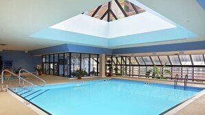 En indendørs swimmingpool med glasvægge, ovenlys og plantekasser.