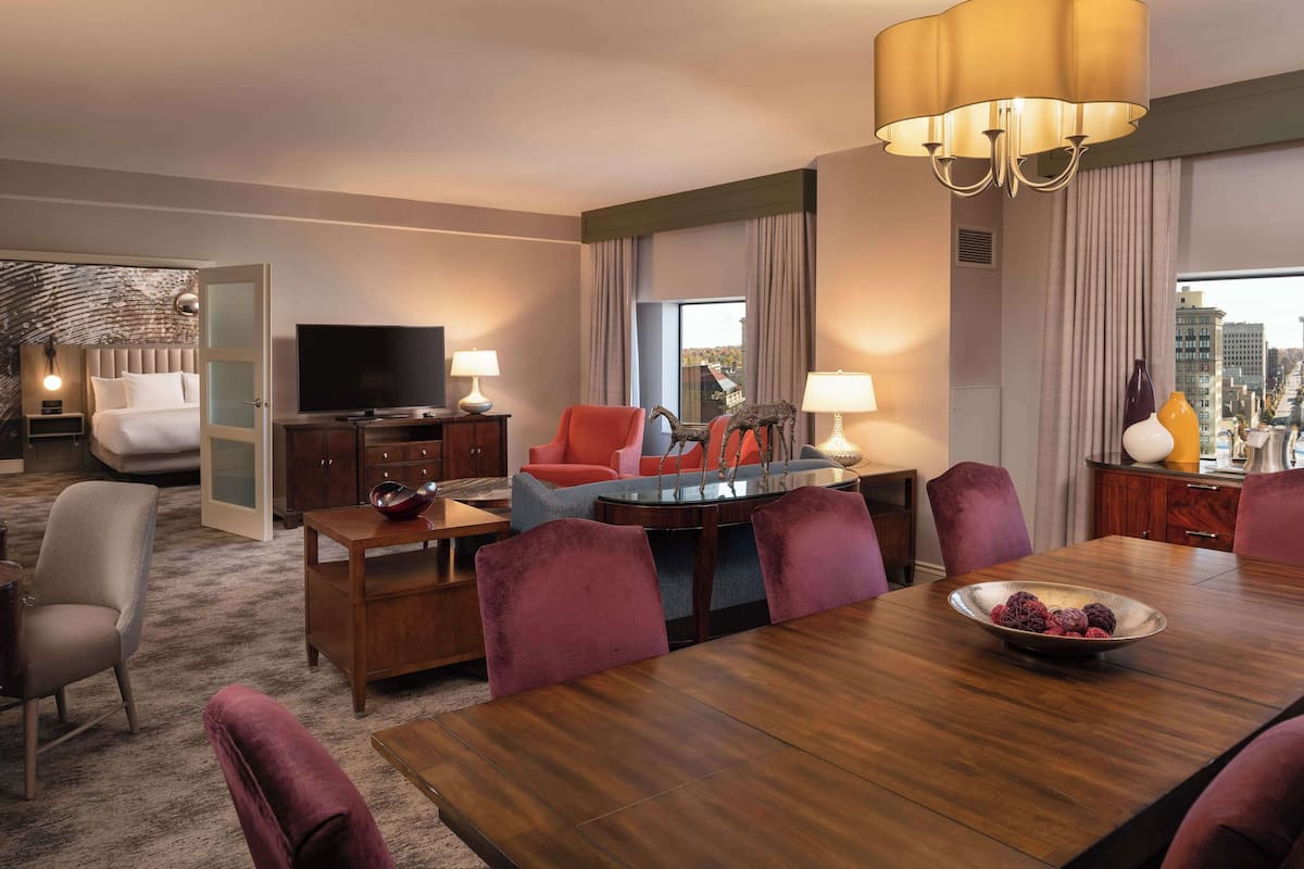 Quarto de hotel com cama, televisão, mesa de jantar, cadeiras e vista para a cidade.