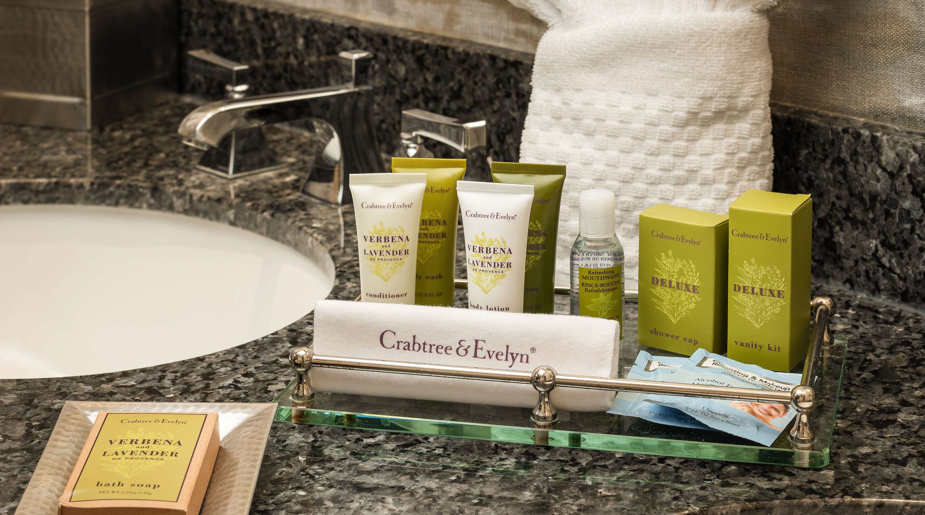 A bathroom vanity with a marble countertop, a sink, and a glass soap dish holding various Crabtree & Evelyn products.