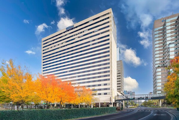 A modern hotel building with a prominent sign, surrounded by autumn foliage and a clear sky.
