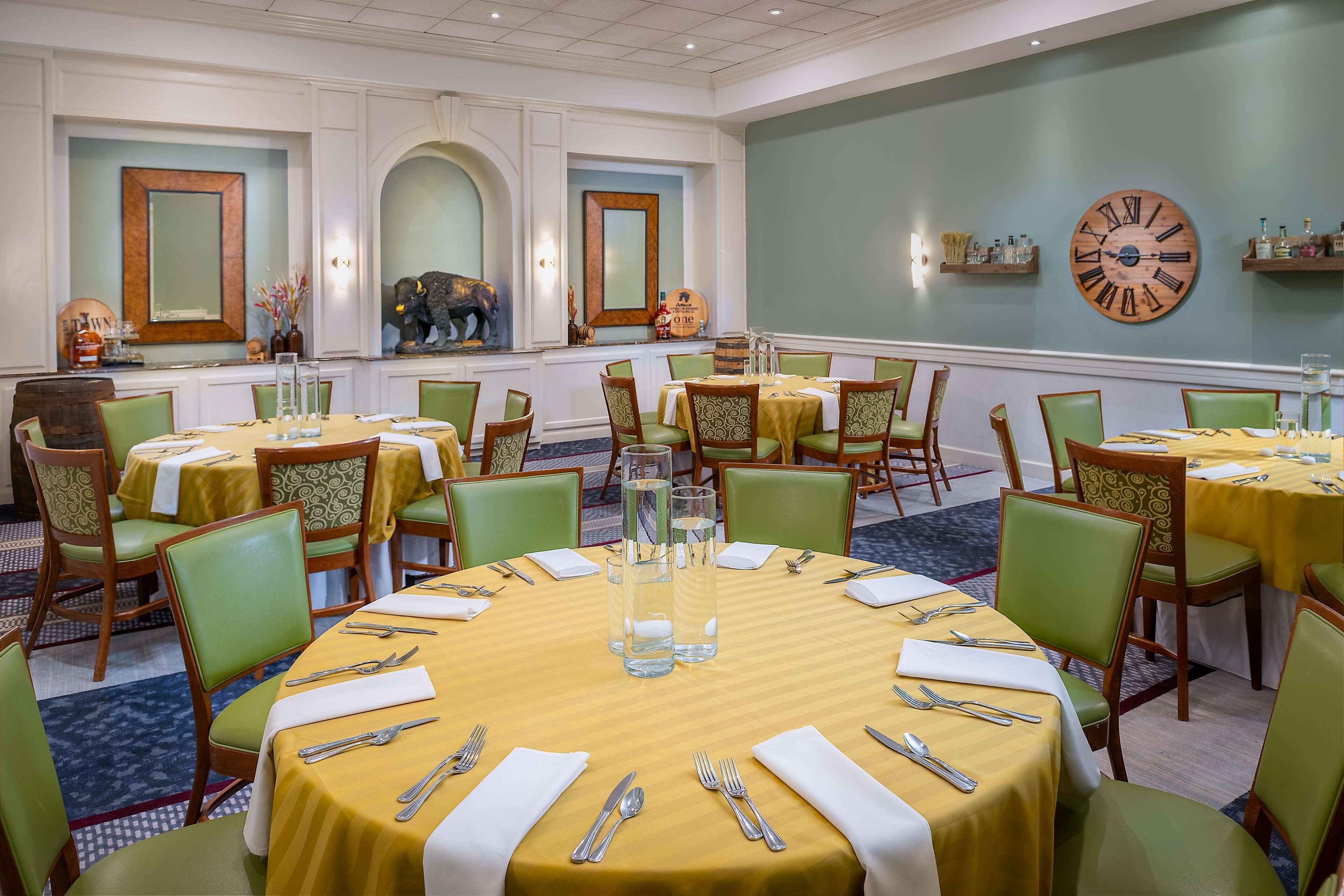 Comedor con mesas redondas, sillas verdes y manteles amarillos.