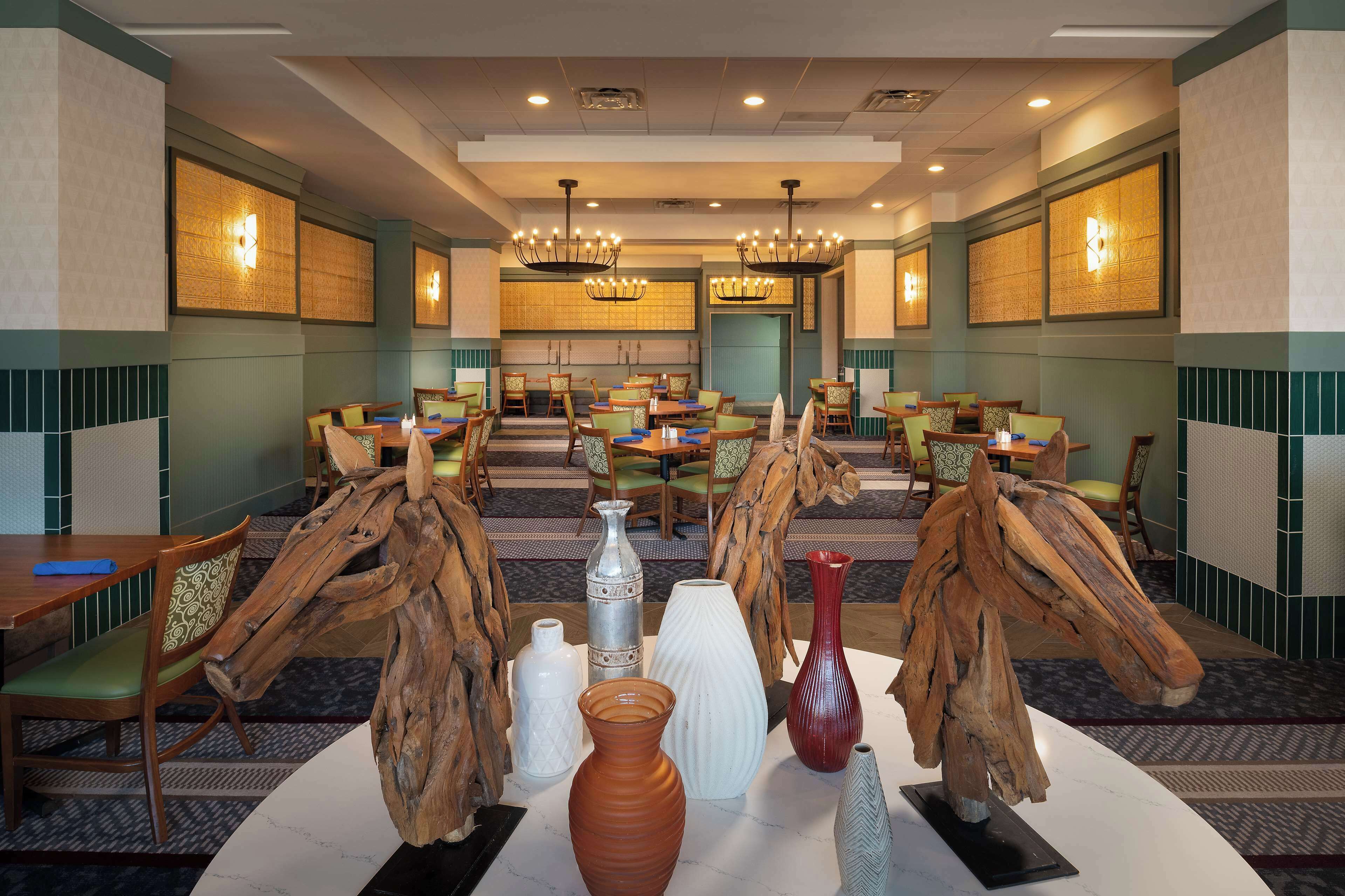 Un hall d’hôtel doté de plusieurs espaces aménagés avec des sièges, des vases en bois et une pièce décorative centrale.