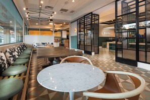 A modern interior with a long communal table, cushioned seating, and a bar area with glass partitions.