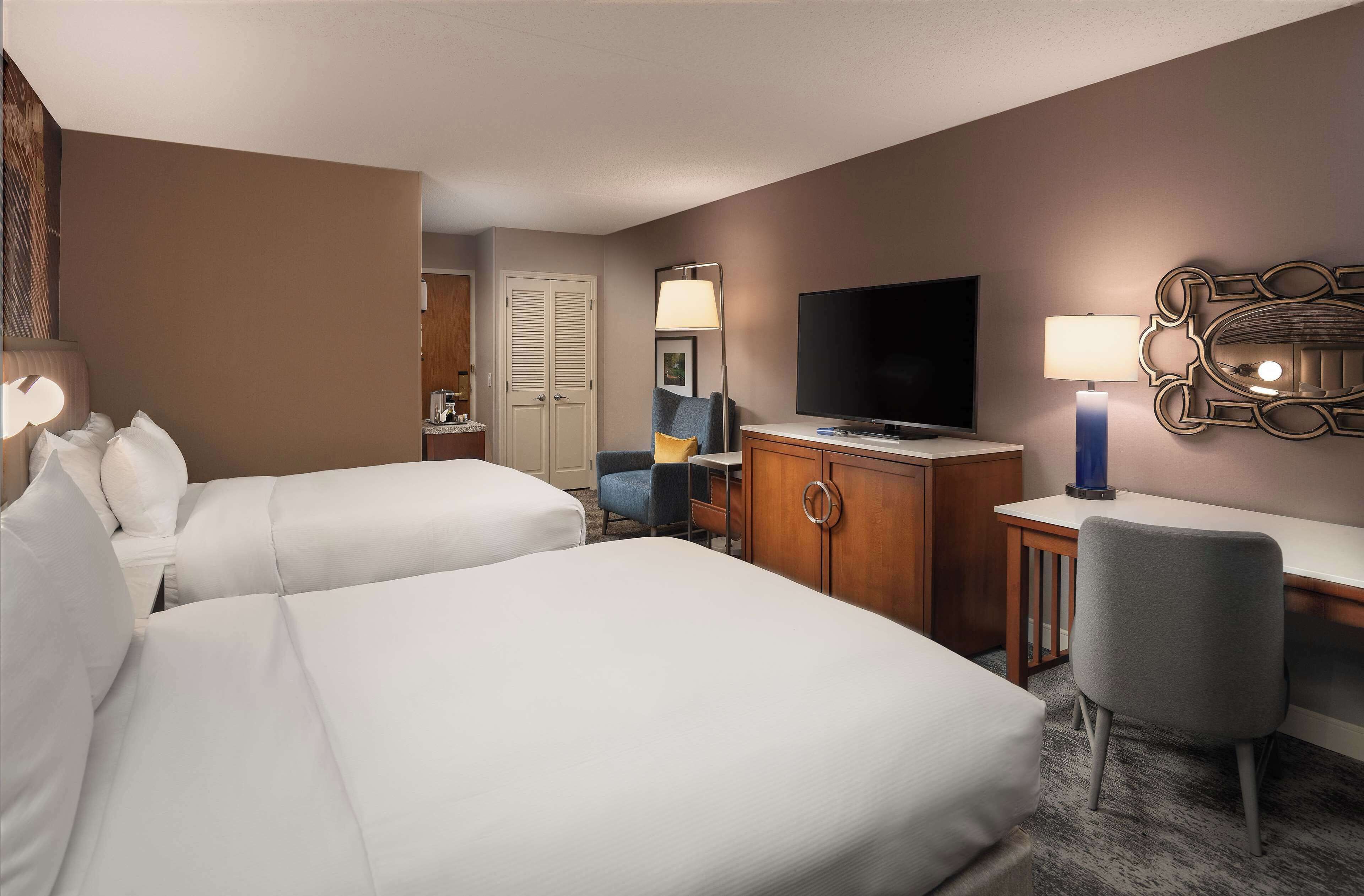 A hotel room with two beds, a desk, a television, and a chair.