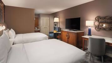 A hotel room with two beds, a desk, a television, and a chair.