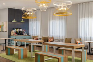 A modern dining area with wooden tables and benches, a coffee station, and large windows with sheer curtains. - Spark by Hilton Toronto Mississauga (Mississauga)