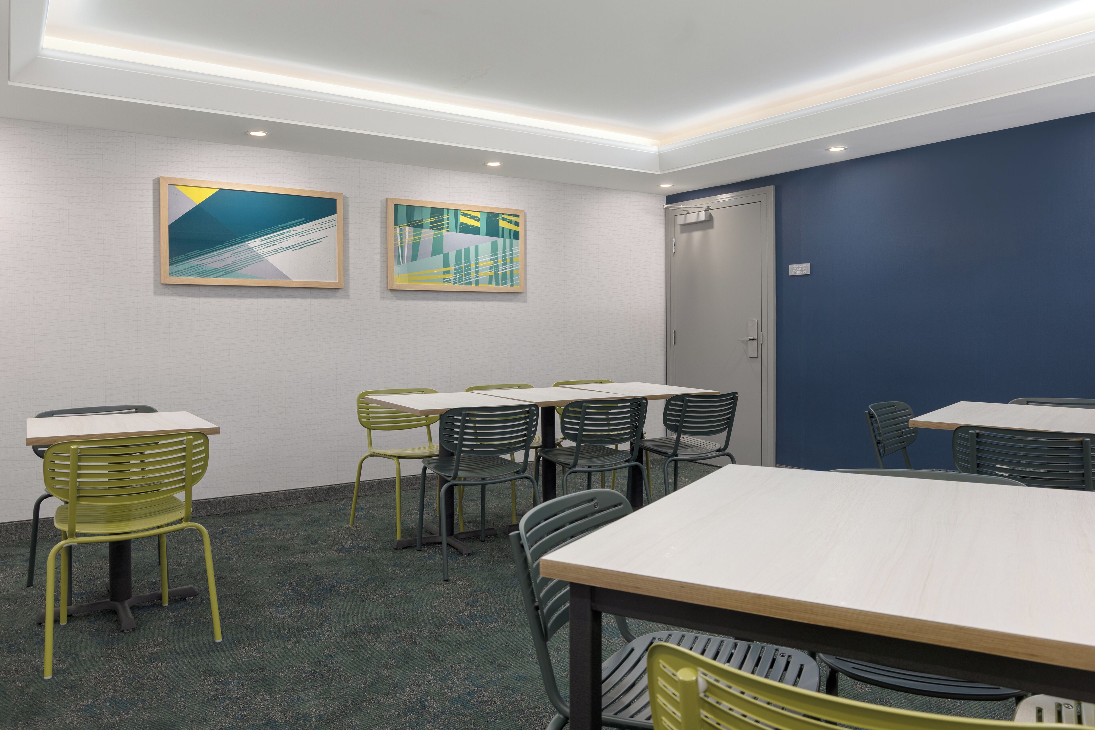 A conference room with tables and chairs, two framed artworks on the wall, and a door to the right.