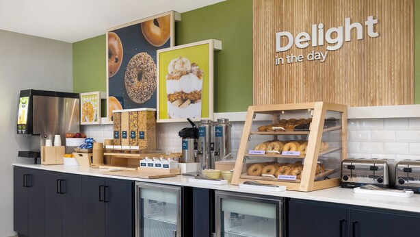 A bakery counter with various baked goods, a coffee machine, and a sign that reads "Delight in the day". - Spark by Hilton Toronto Mississauga (Mississauga)