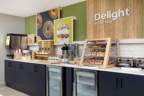 A bakery counter with various baked goods, a coffee machine, and a sign that reads "Delight in the day". - Spark by Hilton Toronto Mississauga (Mississauga)
