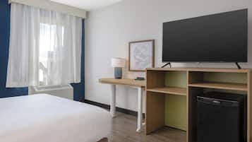 Une chambre d’hôtel équipée d’un lit, d’un bureau, d’une télévision, d’une lampe et d’un petit réfrigérateur.