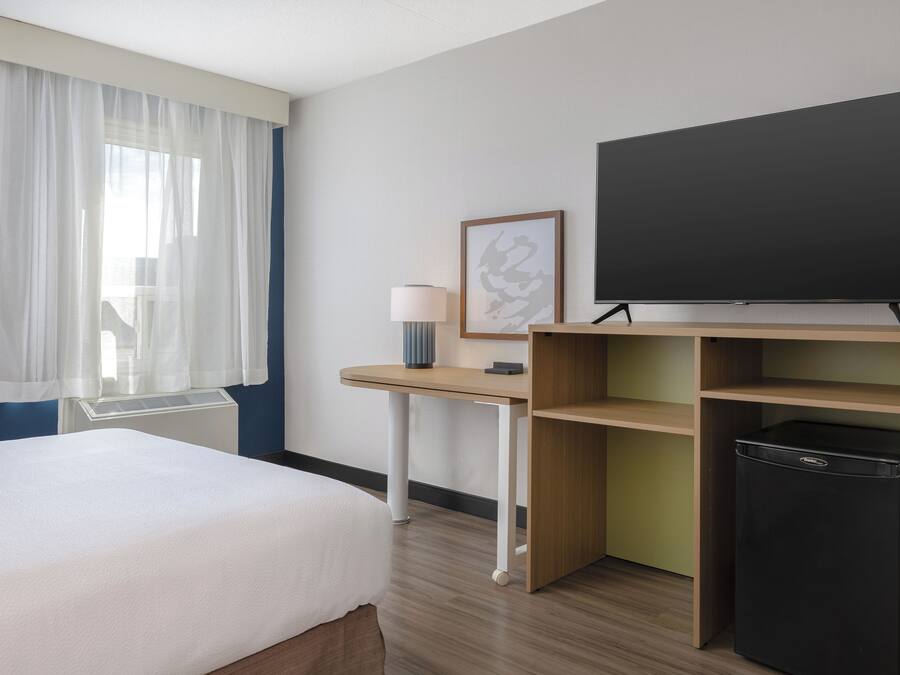 Une chambre d’hôtel équipée d’un lit, d’un bureau, d’une télévision, d’une lampe et d’un petit réfrigérateur.
