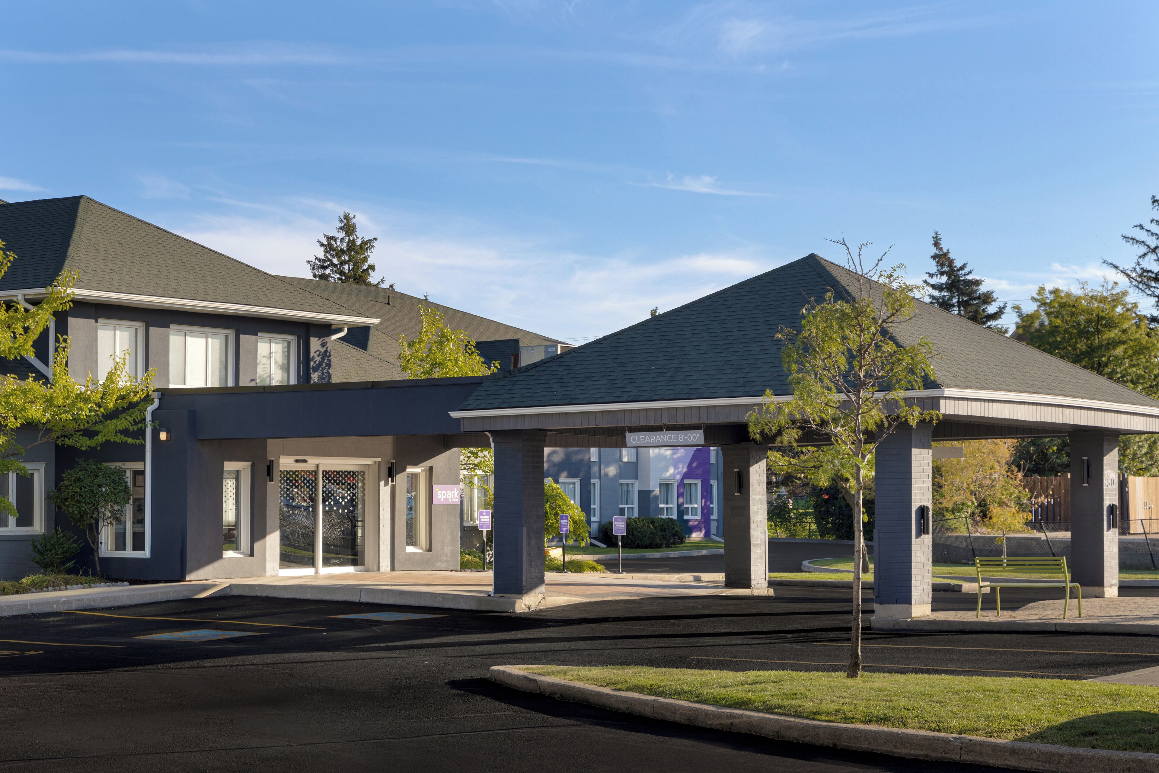 A modern building with a covered entrance, a parking lot, and a grassy area with a bench.