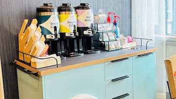 A coffee station with a vintage cart, two coffee dispensers, a hot water dispenser, and a small selection of condiments and napkins.