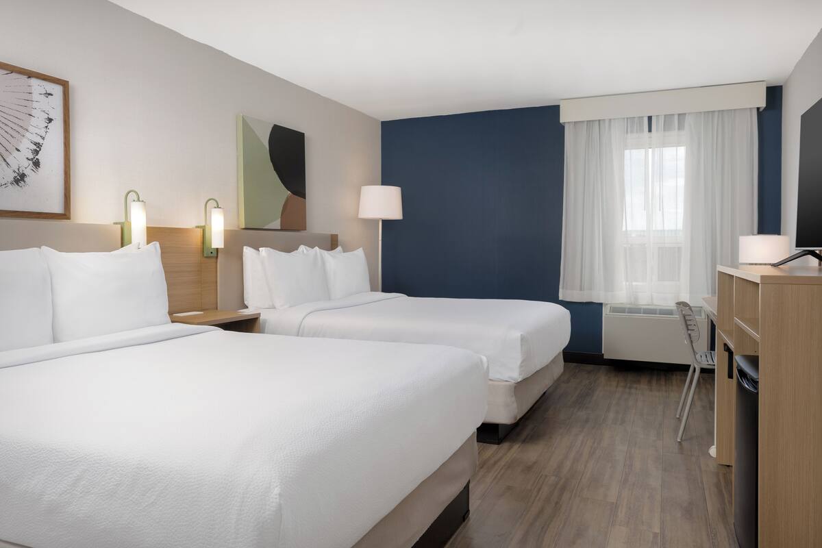 A hotel room with two beds, a desk, a chair, a lamp, and a window with curtains.