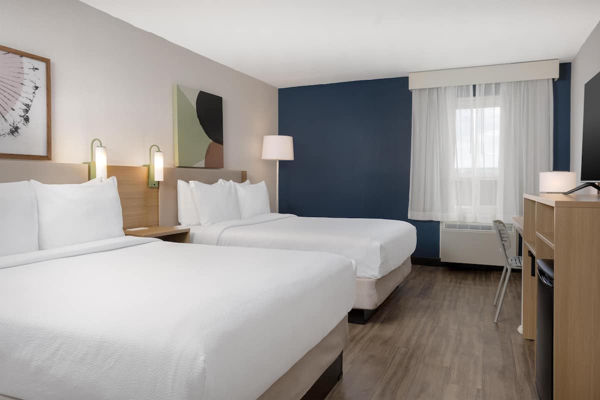 A hotel room with two beds, a desk, a chair, a TV, and a window with curtains.