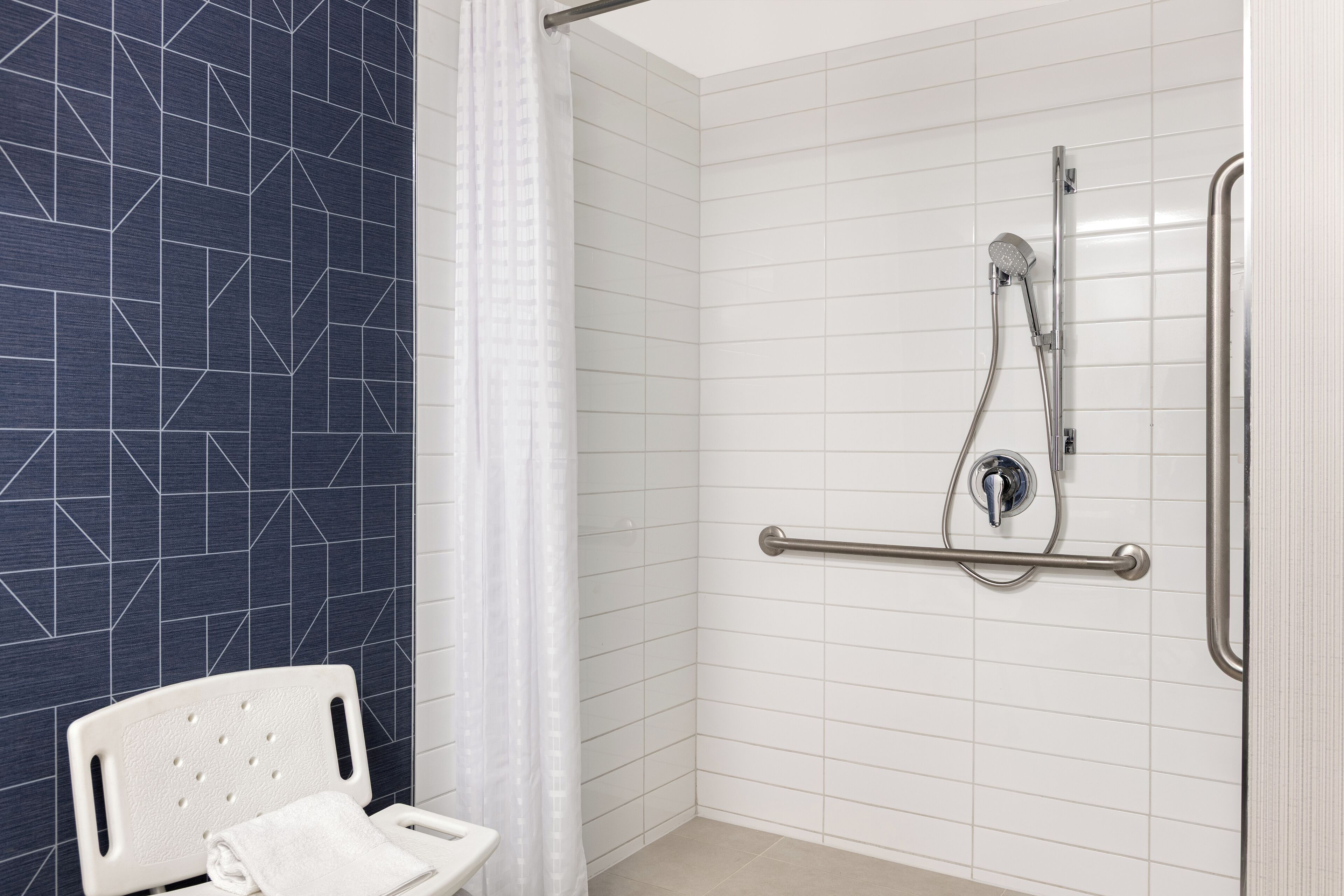 A bathroom with a shower, a white toilet, and a white chair.
