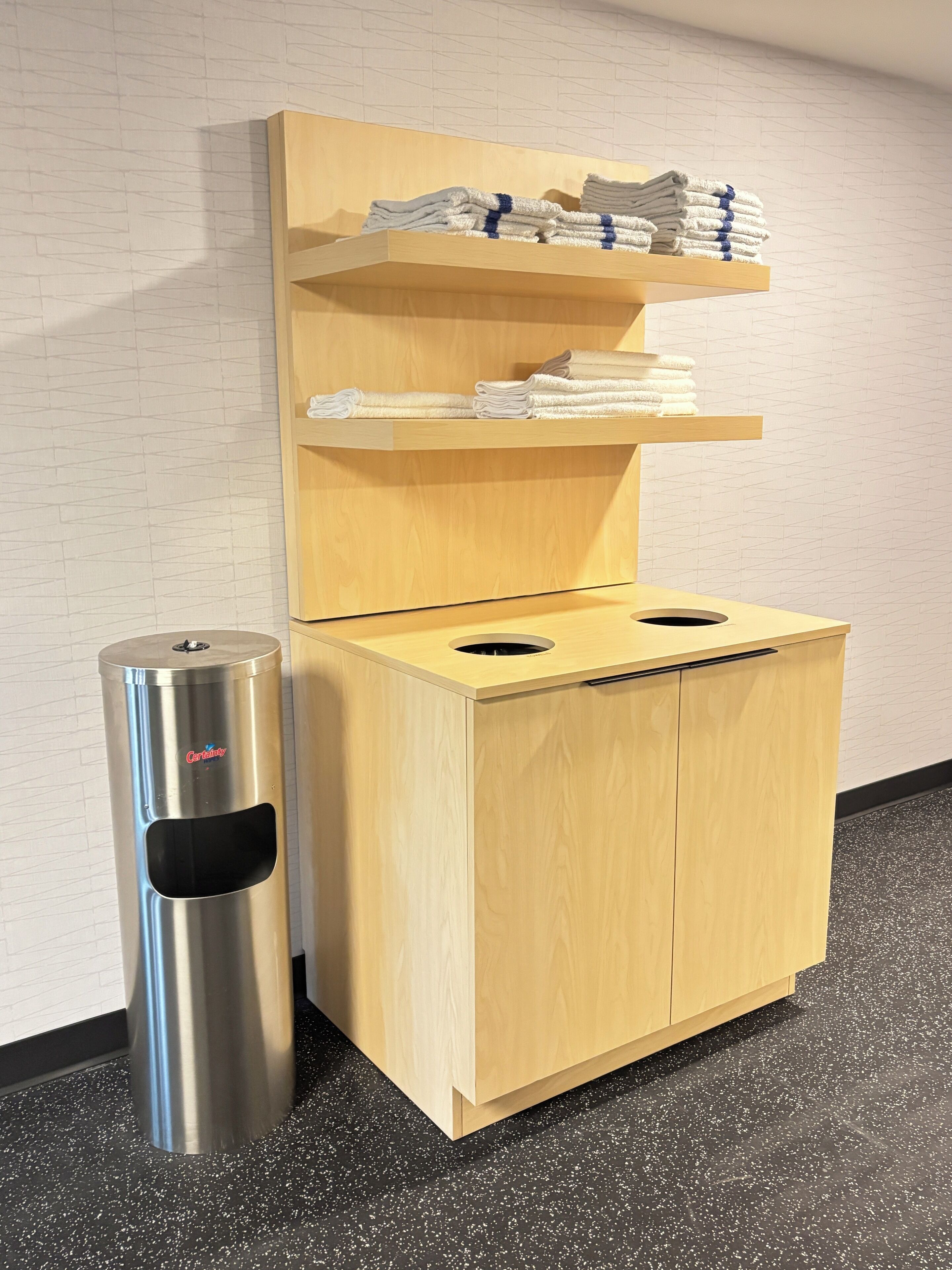 A compact, modern bathroom with a wooden cabinet, a stainless steel trash bin, and a towel rack.