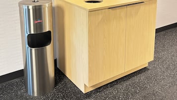A compact, modern bathroom with a wooden cabinet, a stainless steel trash bin, and a towel rack.