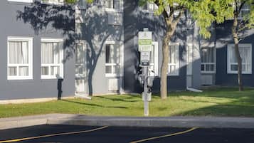 Een parkeerbord voor elektrische voertuigen en een laadstation voor een gebouw met meerdere ramen en een boom.