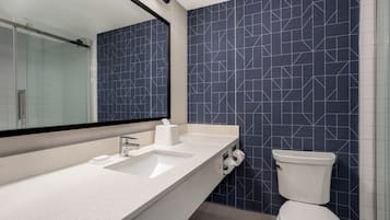 Casa de banho moderna com bancada branca, um espelho grande e sanita com painel de azulejos geométricos azuis.