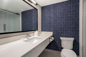 A modern bathroom with a white countertop, a large mirror, and a toilet with a blue geometric tile backsplash. - Spark by Hilton Toronto Mississauga (Mississauga)