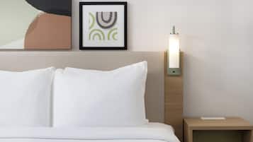 A neatly made bed with white linens, a framed abstract artwork above it, and a bedside table with a lamp.