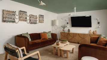 A modern living room with a brown sofa, a wooden chair, a coffee table, and a TV mounted on the wall.