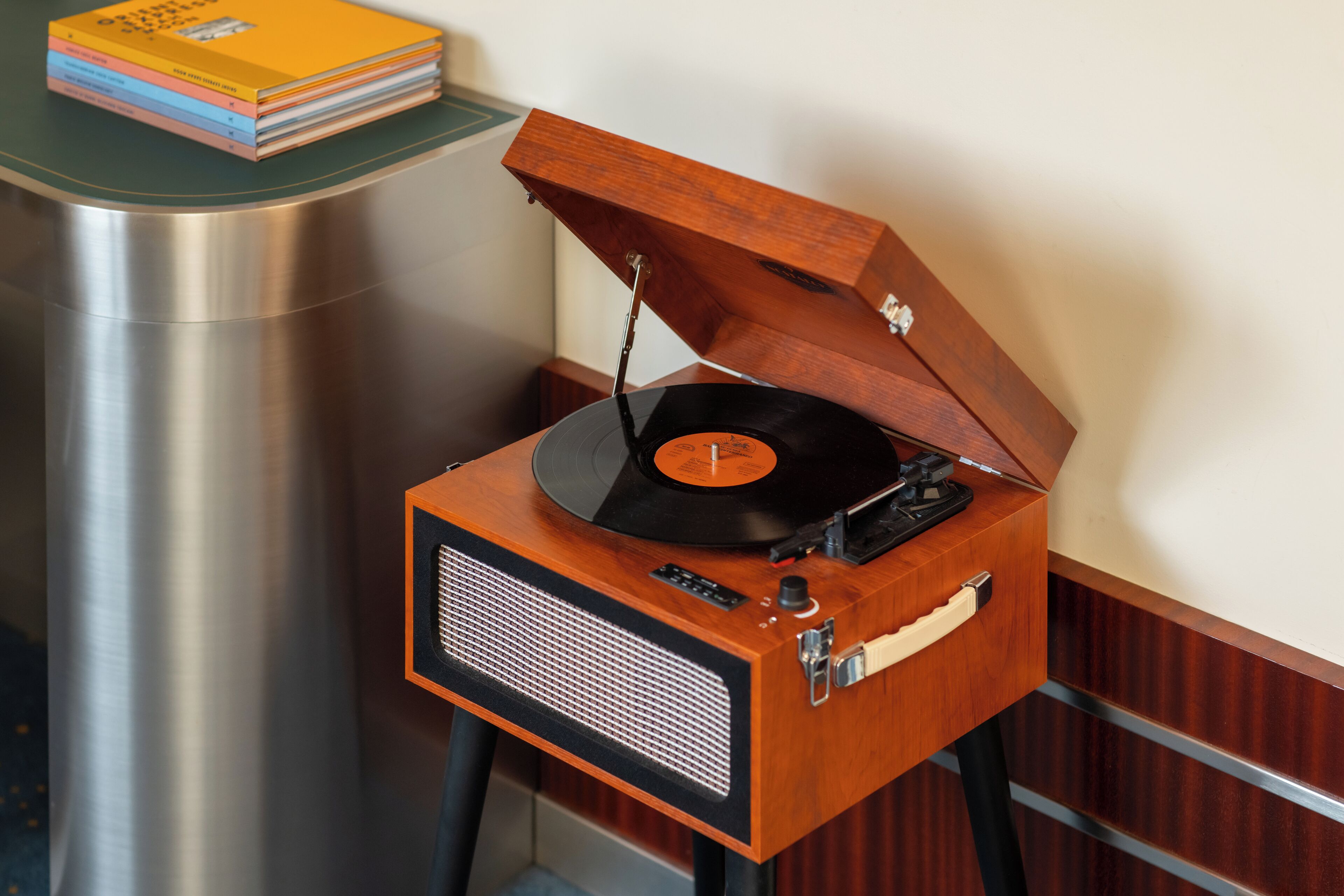 A vintage wooden record player on a small table with a stack of colorful books on a green surface beside it.