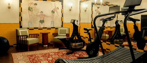 A gym with exercise equipment, a patterned rug, and a wall with a fitness-themed painting.