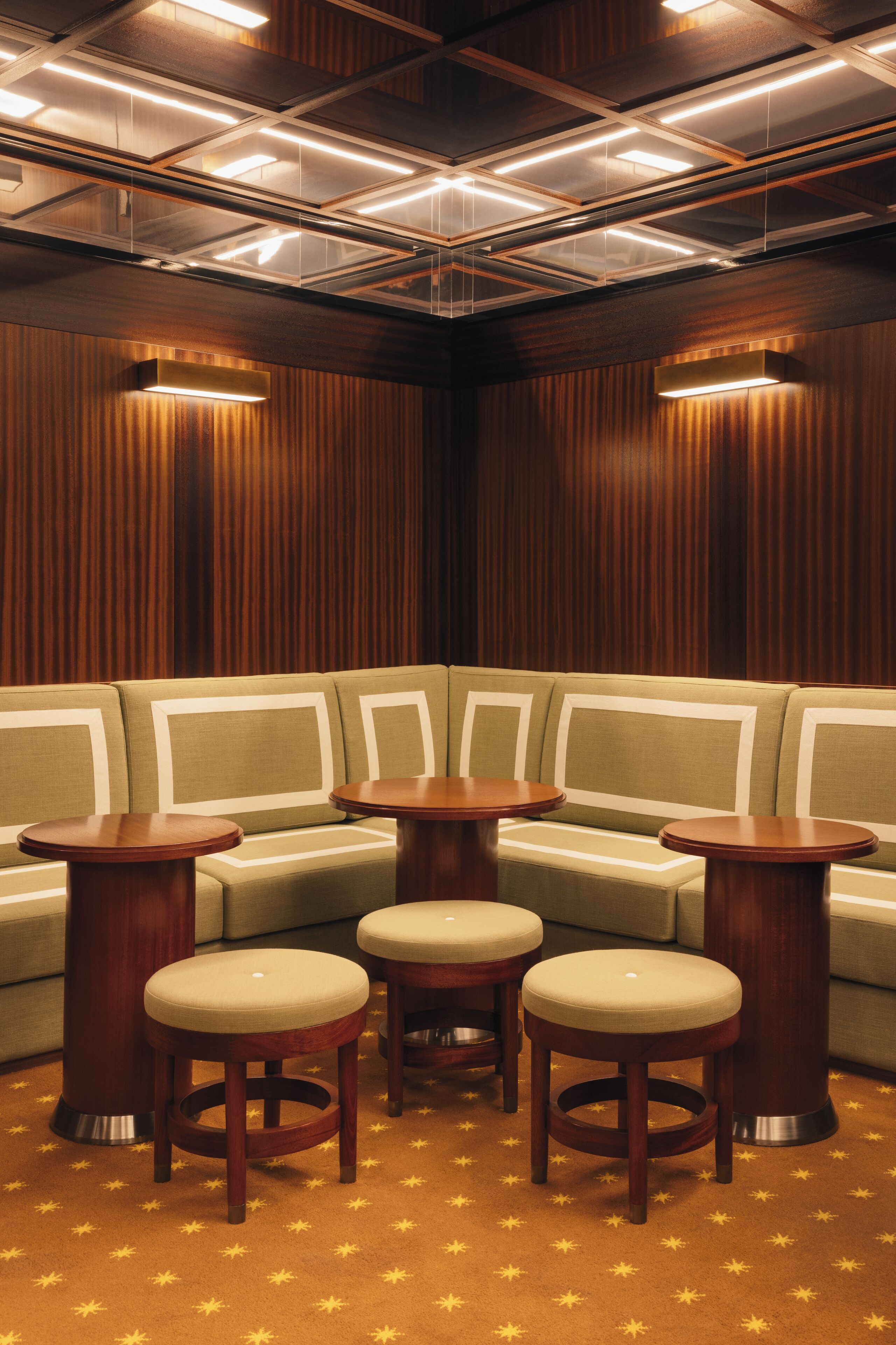 A corner seating area with a sofa and three wooden stools, a ceiling with recessed lighting, and a patterned carpet.