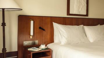 A hotel room with a wooden headboard, a bedside table with a lamp, a framed artwork on the wall, and a bed with white bedding.