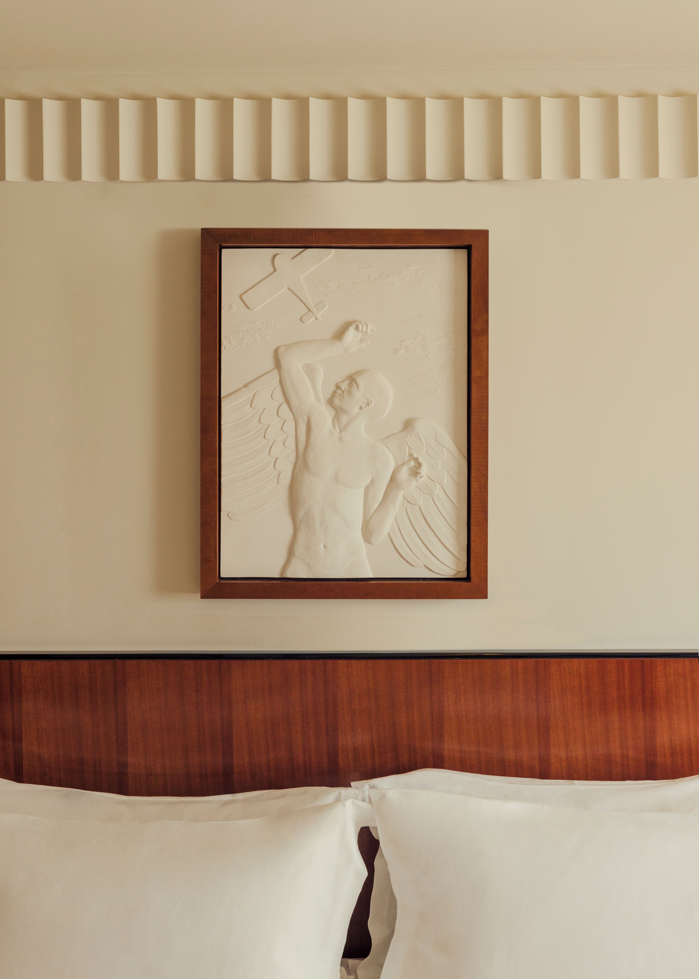 A framed bas-relief sculpture of a winged figure on a wall above a wooden headboard.